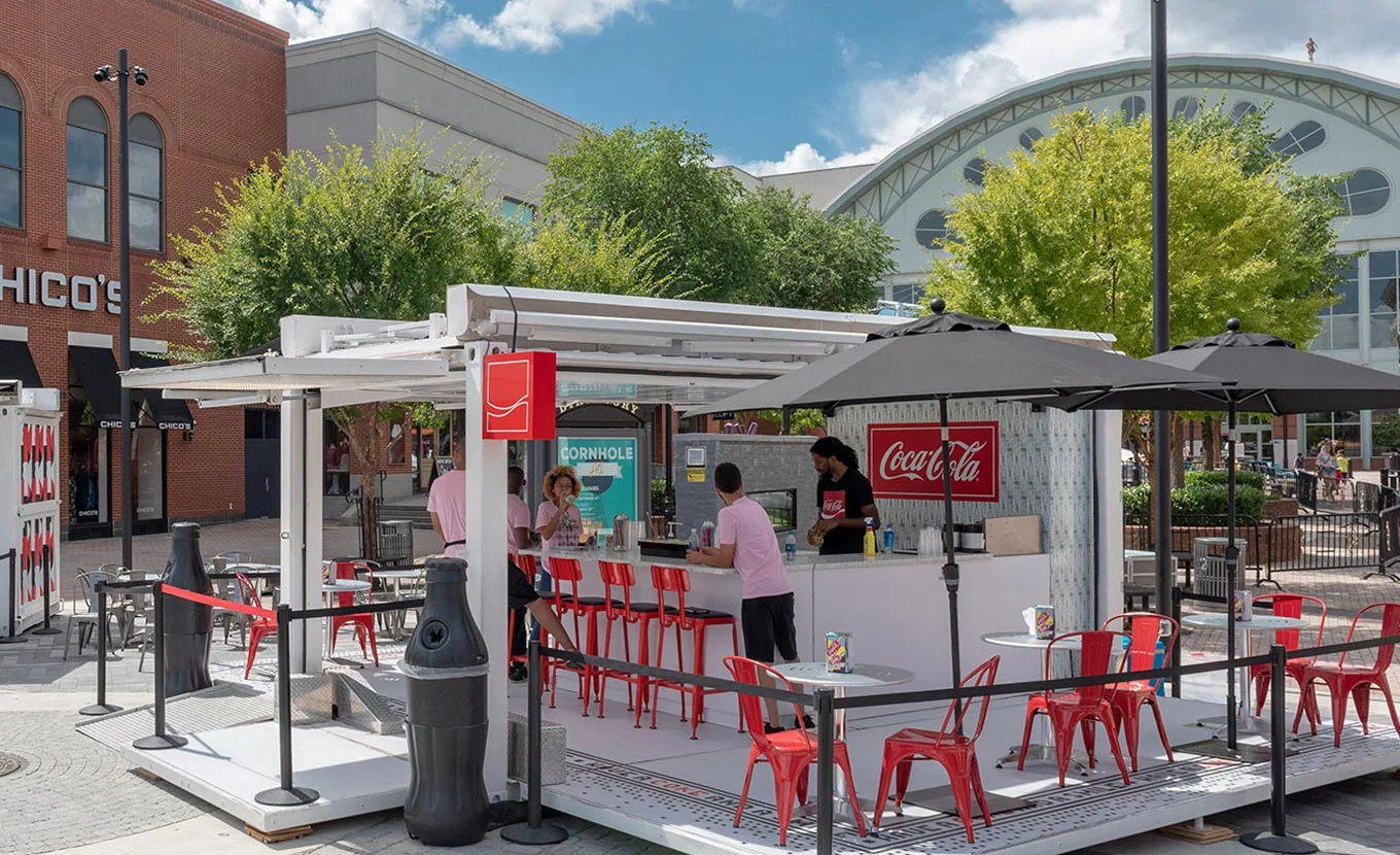 Coca-Cola branded portable bar with a bartender, red stools and bottle-shaped bollards