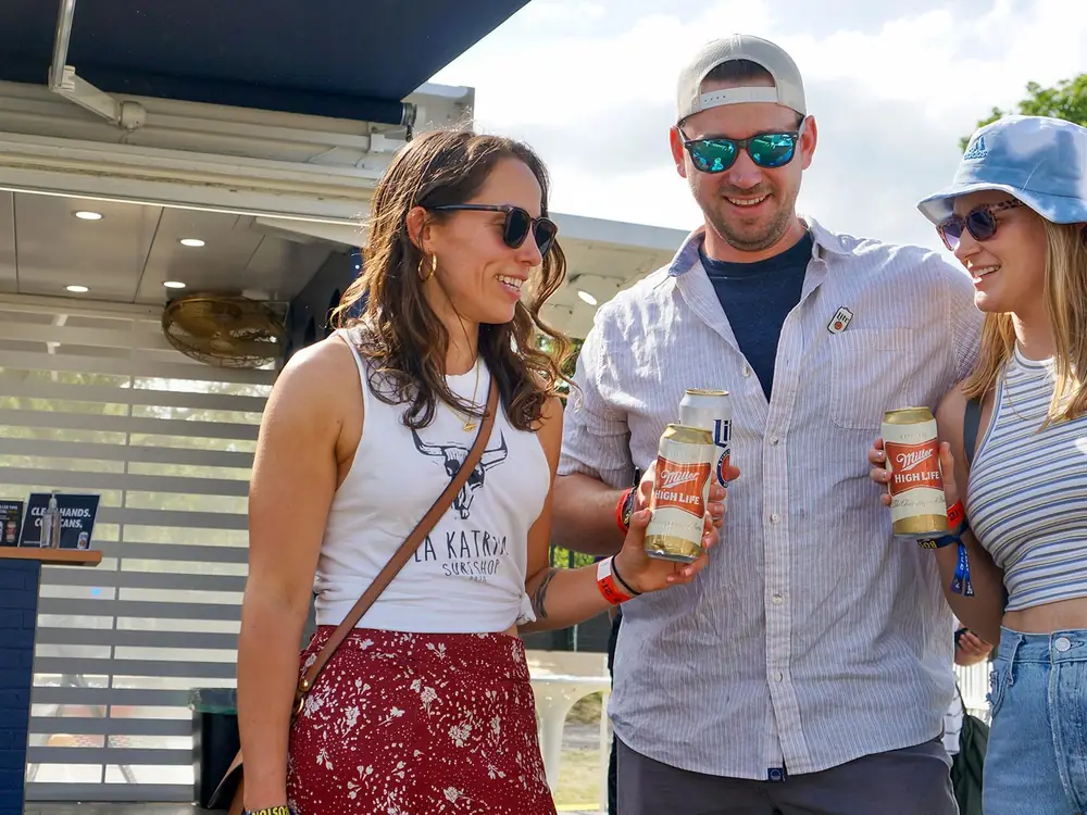 Festival-goers holding drinks in front of the Miller Lite bar